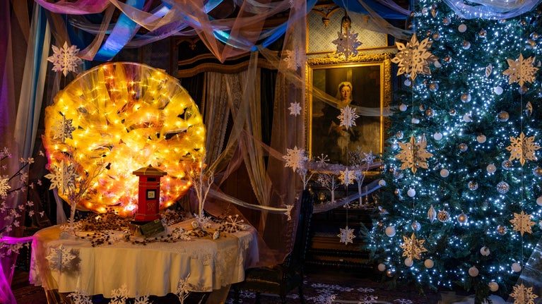 Christmas tree decorated in white lights and snowflakes. The dining room table has a post box and a fabric sun flowing with warm light.